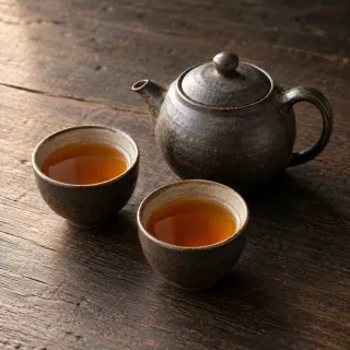 A small unbranded ceramic teapot and two cups of amber tea on a wooden table