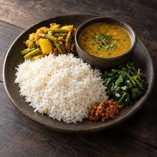 A vegetarian Nepali dal bhat plate: white rice, lentil dal in a small bowl, seasonal vegetable curry, leafy greens and a little pickle
