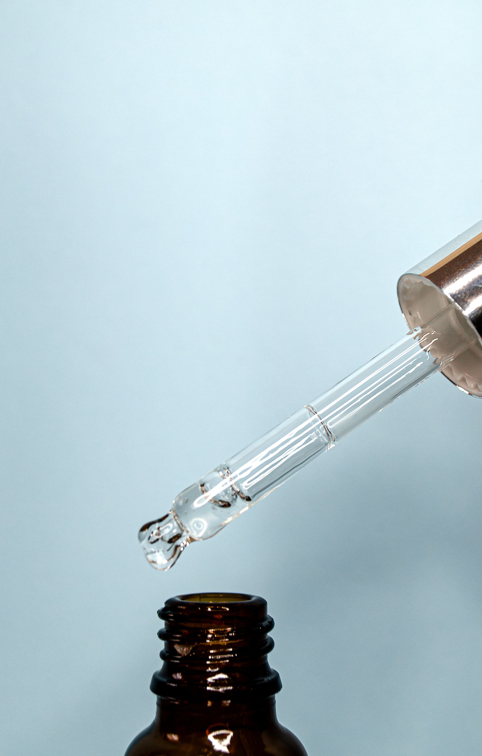 Clear dropper poised above an unlabelled amber glass bottle