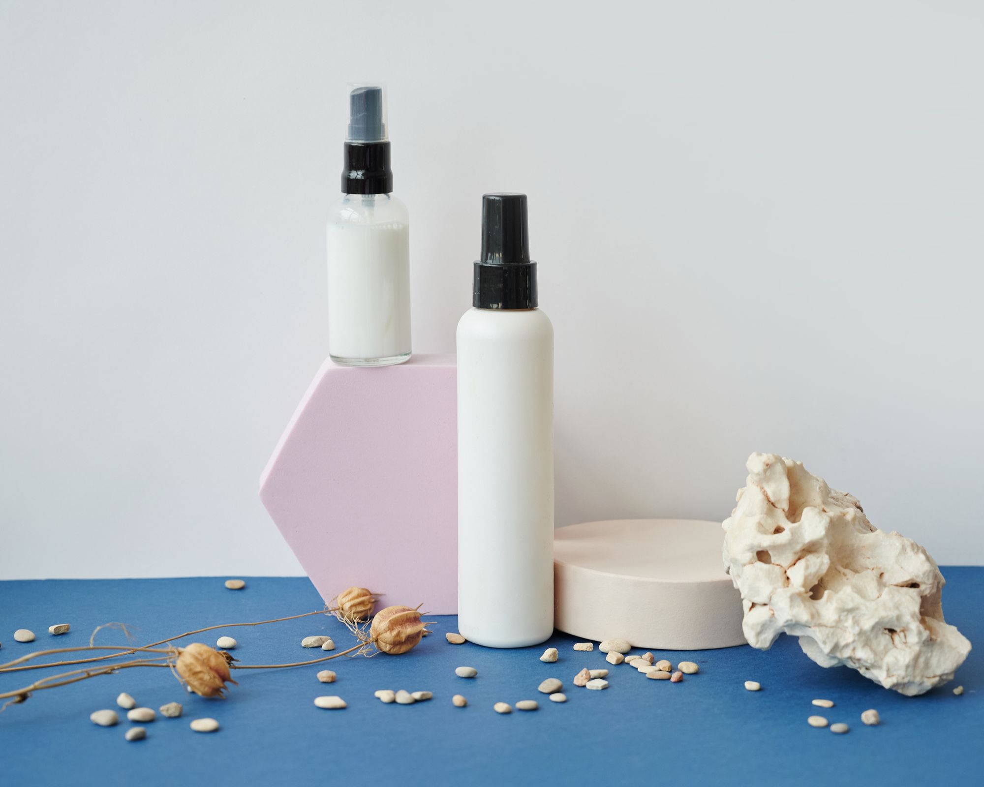 Blank cosmetic bottles arranged with stones on a blue surface