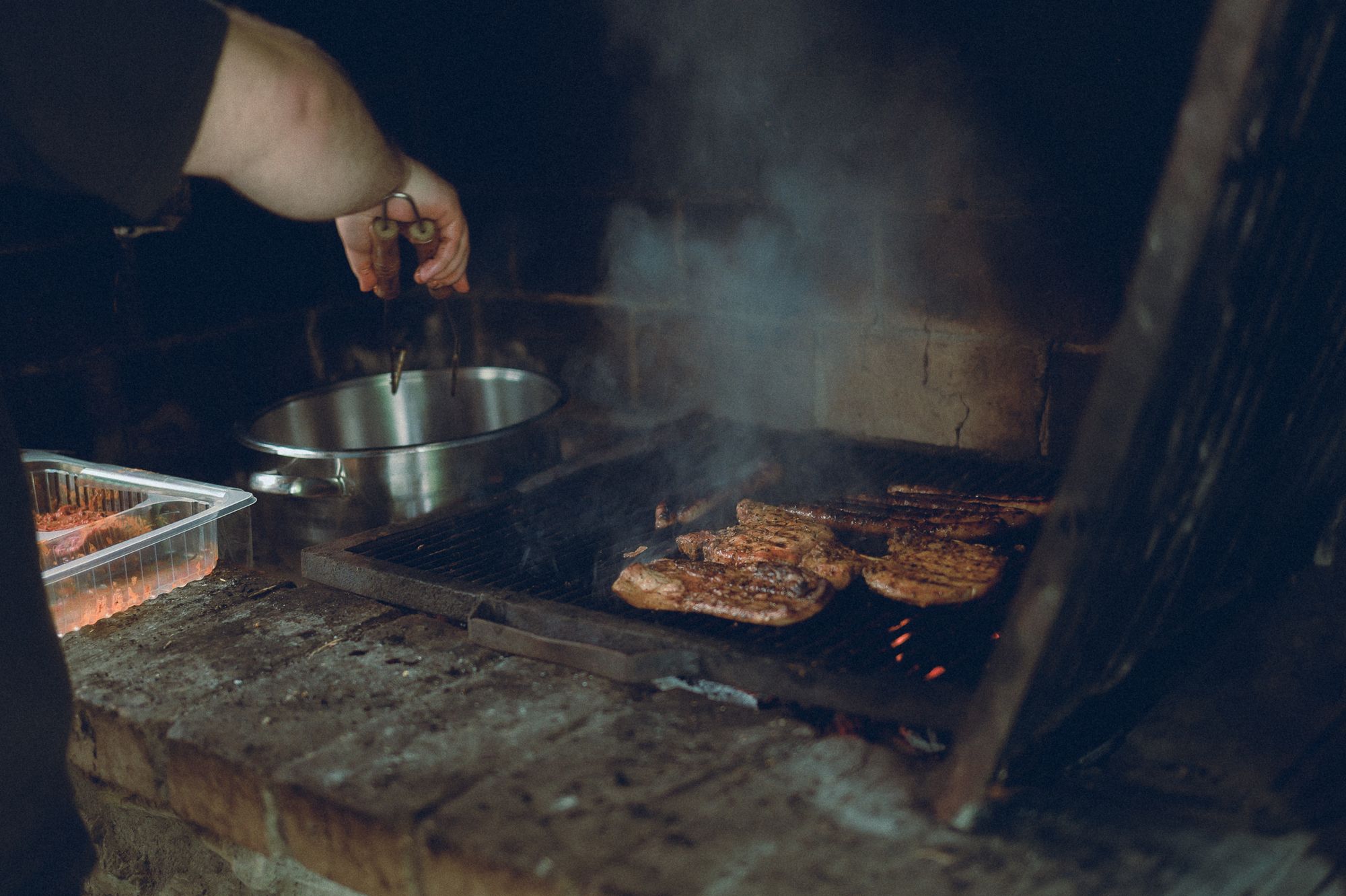 Cook tending meat above a charcoal grill
