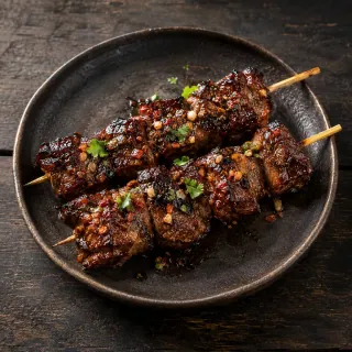 Two skewers of boneless grilled buffalo short-rib pieces, dark soy recado glaze, smoked chilli and fermented garlic
