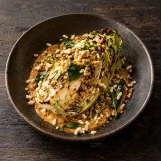 A grilled pointed cabbage wedge on peanut satay, lime leaf and puffed rice