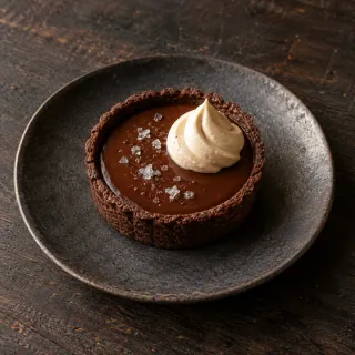 One small dark chocolate tart with smooth chocolate filling, a fine sprinkle of smoked salt and a small swirl of malted-soy cream