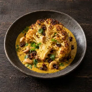 A roasted cauliflower half over yellow curry mole with a few raisins and cashews