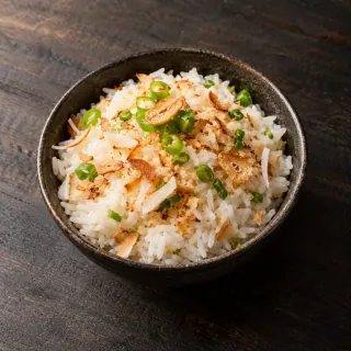A small bowl of white coconut rice topped with scallion, toasted coconut and crisp garlic