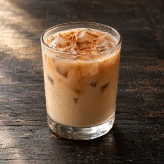 A chilled light tan rice-milk horchata with cold-brew coffee, visible small ice cubes and a light cinnamon dusting in a simple plain glass. No dairy jug or coffee beans