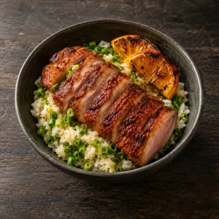 A bowl of scallion rice topped with crisp-skinned achiote duck slices and charred orange