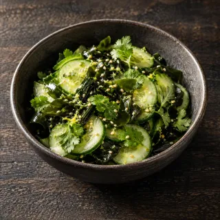 A small bowl of crisp cucumber slices and dark green wakame seaweed, citrus dressing, sesame and coriander