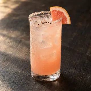A chilled pale-pink grapefruit and tequila Paloma in an unbranded clear highball glass, realistic ice cubes, fine timur-salt rim and a small grapefruit slice