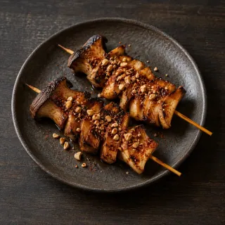 Two skewers of lengthwise sliced grilled king oyster mushrooms, tamari glaze, aji panca and smoked cashew