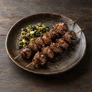 Two skewers of small cooked lamb-heart pieces, cumin, black lime and scallion relish