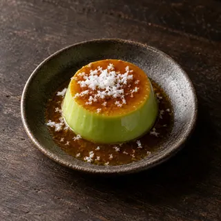 A small glossy pale-green pandan custard flan with palm caramel and a little finely grated coconut