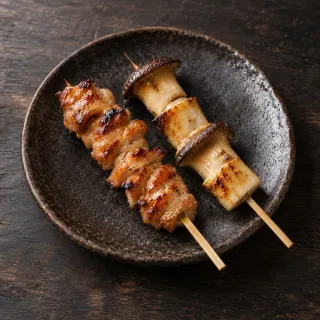 A small plate with exactly one chicken yakitori skewer and one king oyster mushroom skewer