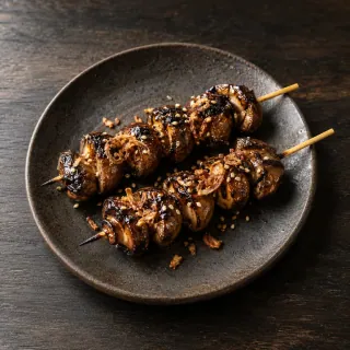 Two skewers of grilled brown mushrooms glazed with black garlic and sesame tare, crispy shallot