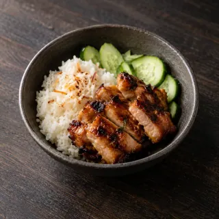 A small bowl of coconut rice with grilled sticky chicken pieces and fresh cucumber