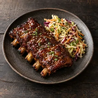 A small rack of cooked pork ribs with glossy tamarind barbecue glaze, sesame slaw alongside