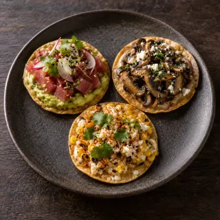 Exactly three small flat corn tostadas on one plate: one tuna and avocado, one mushroom, one charred corn