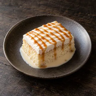 A small rectangular slice of moist vanilla tres leches milk cake with light cream and caramel