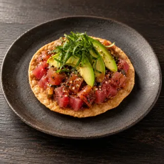 One crisp flat corn tostada with raw diced tuna, gochujang citrus dressing, sliced avocado and shiso
