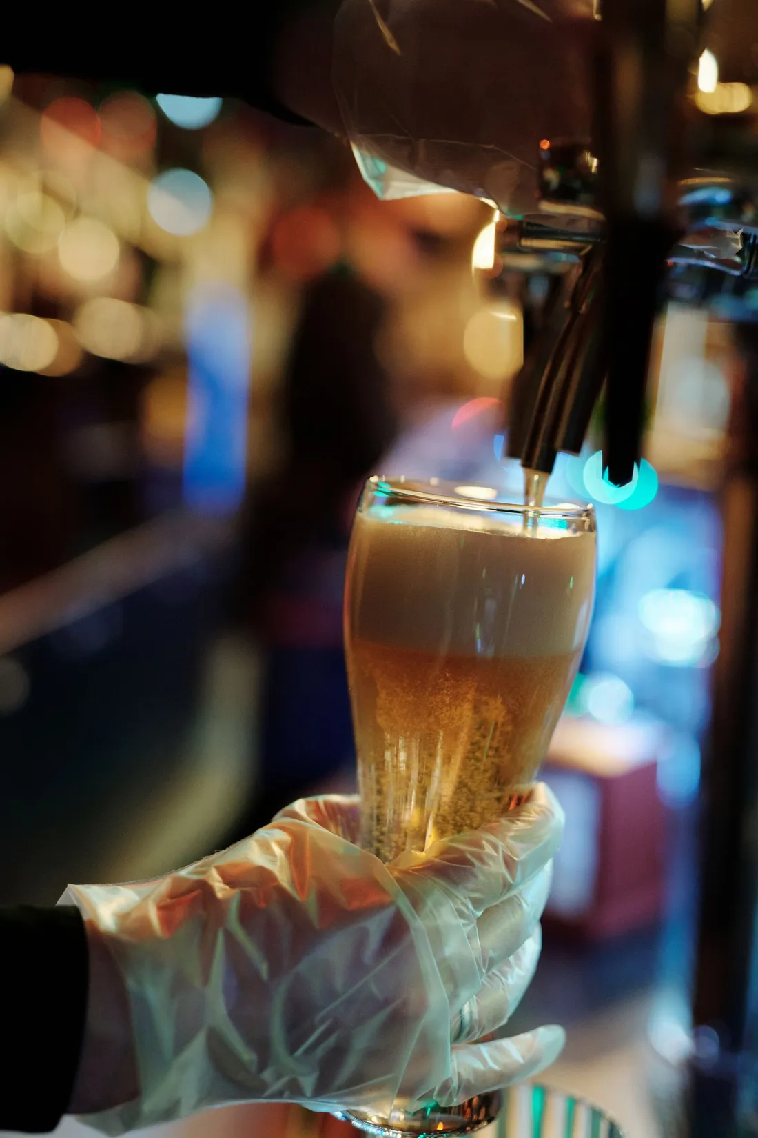 A gloved hand holding a full pint glass beneath brass taps