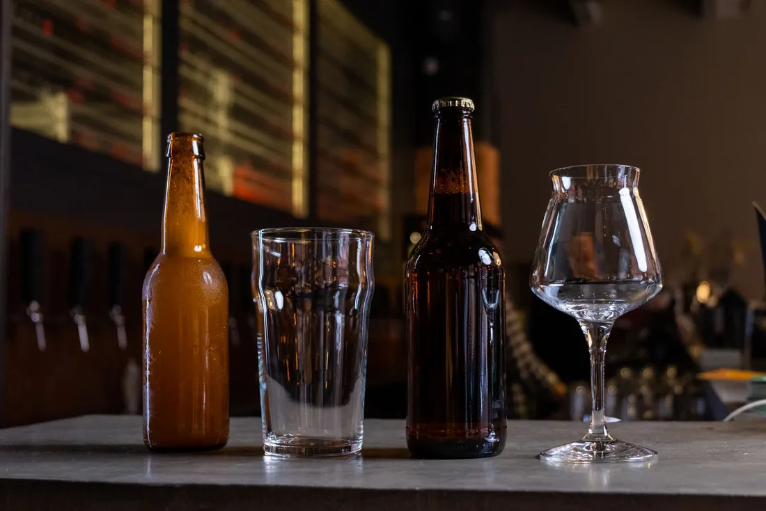 Two unlabeled beer bottles and an empty pint glass on a bar counter