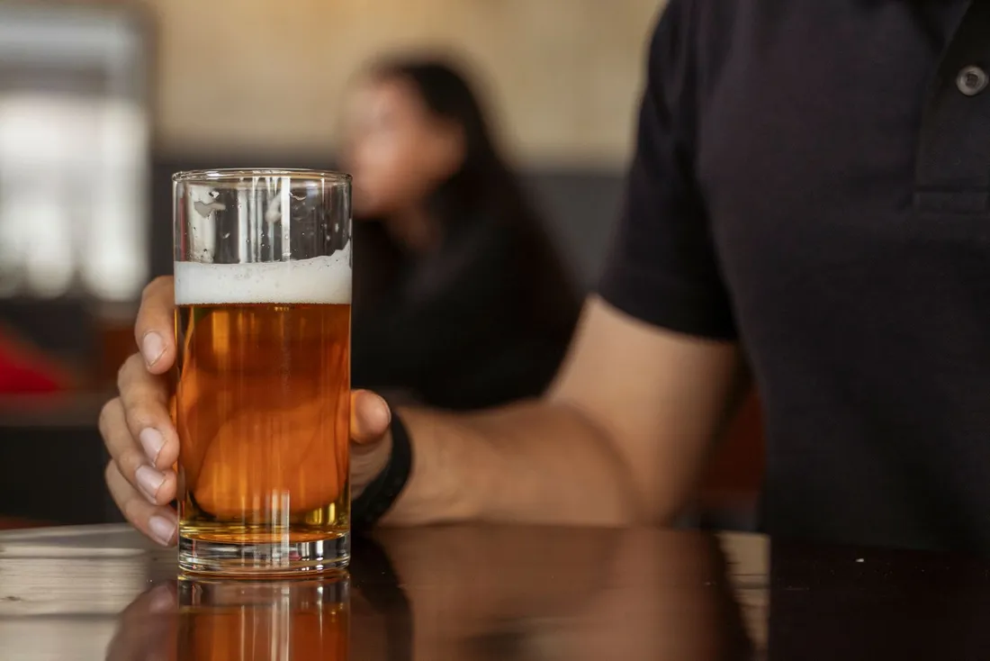 A hand holding a glass of amber beer up against the sky
