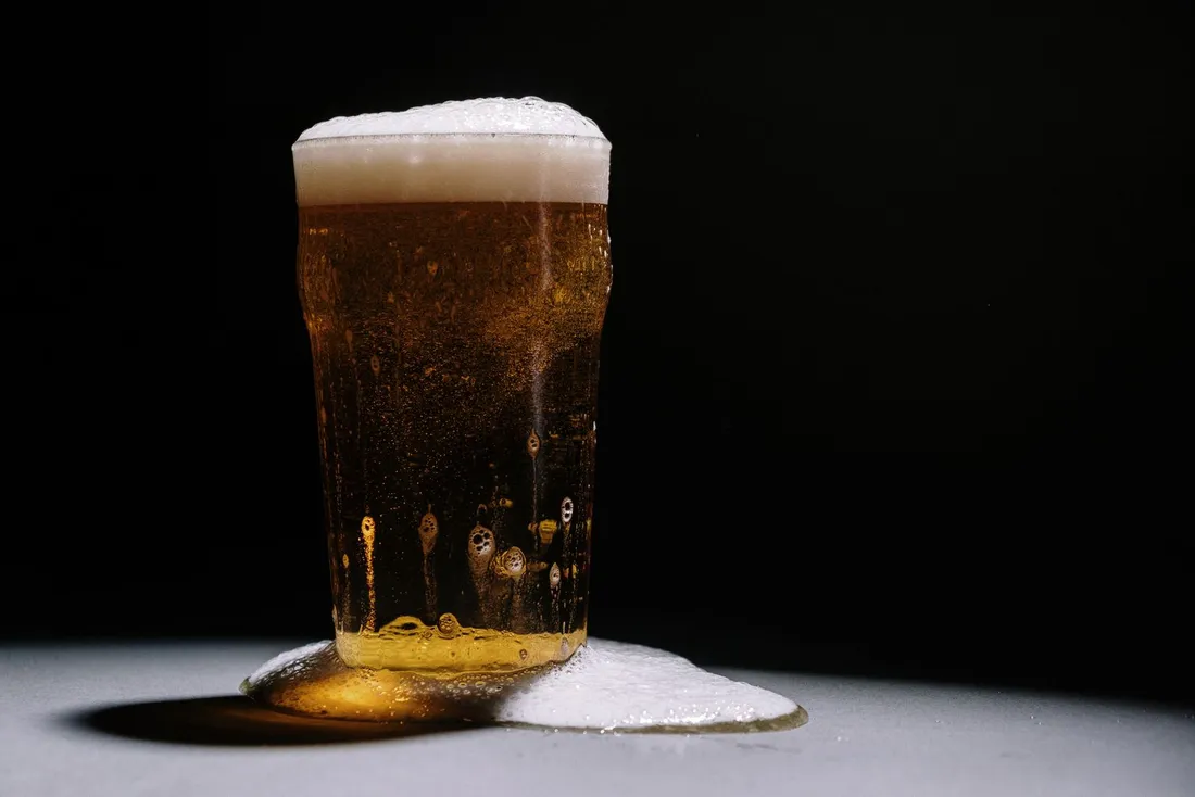 An overflowing glass of golden beer against a black background