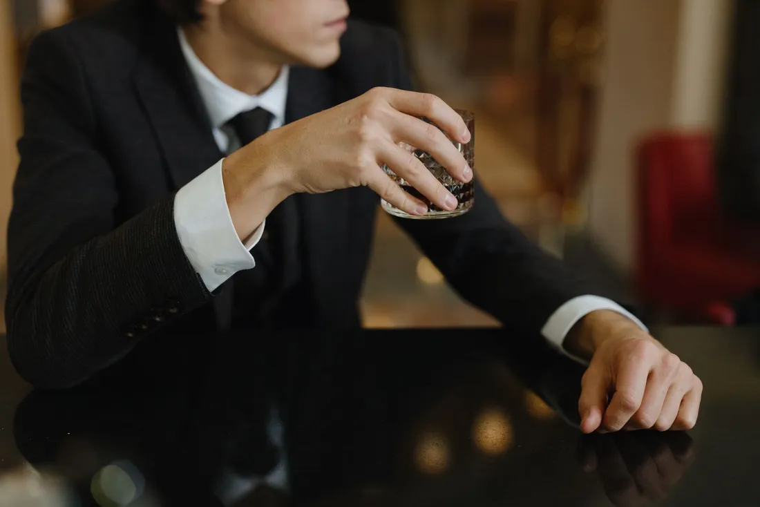 A person in a suit holding a glass of whisky