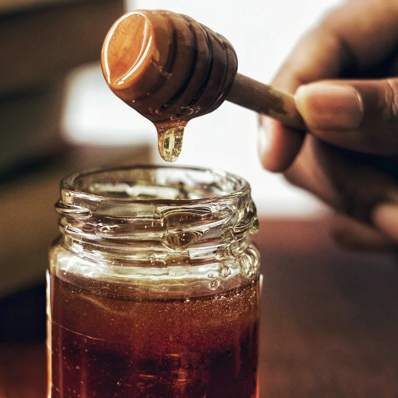 Glass jar of golden raw wildflower honey with wooden dipper