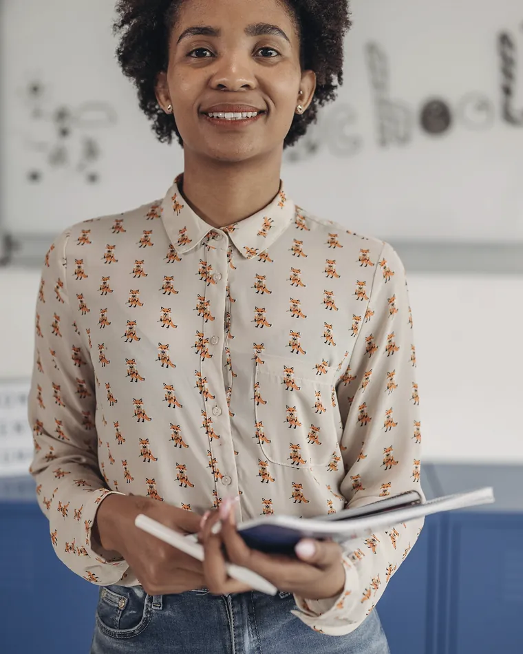 A teacher standing against the studio's pale wall, notebook in hand