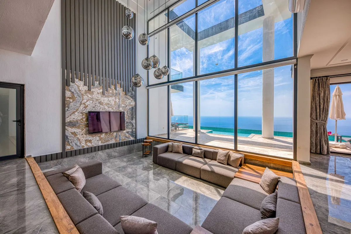 The double-height great room, fireplace wall and floor-to-ceiling glass onto the pool and sea