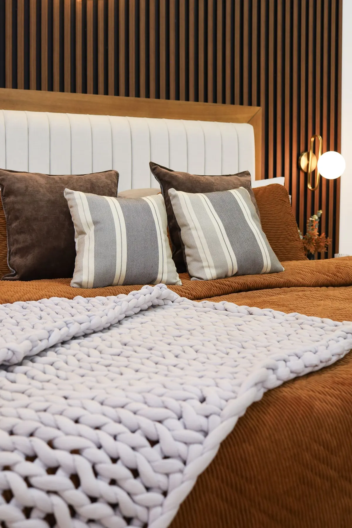 Primary suite detail: wood-slat headboard, brass sconce, warm terracotta bedding