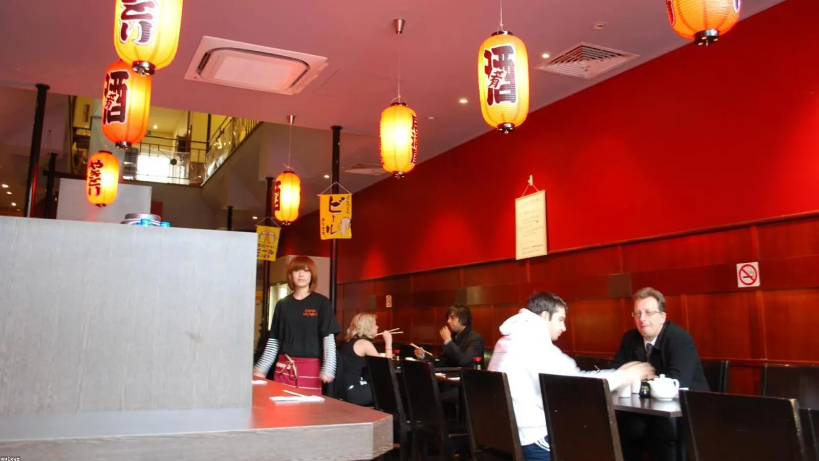 The NORI counter at dusk — eight cypress-wood seats arranged in a single line facing the open kitchen