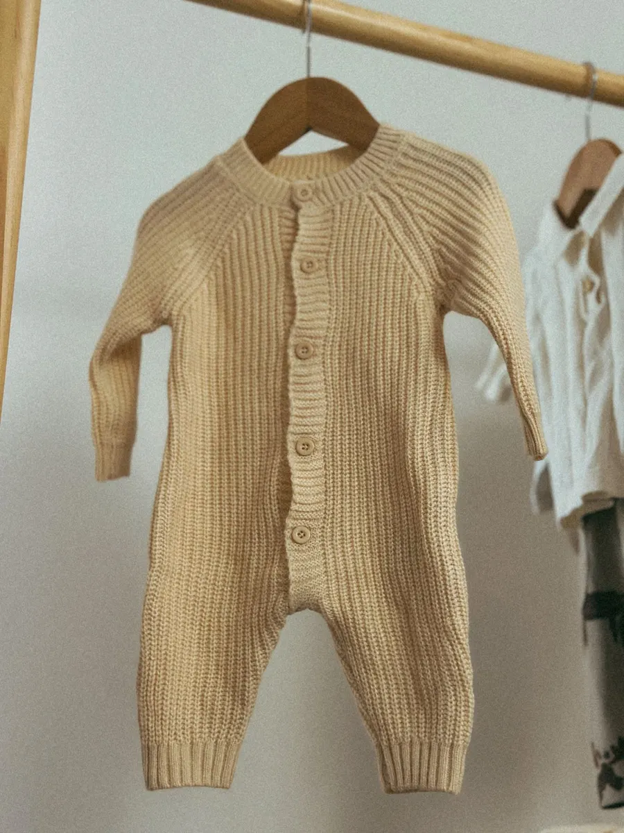 A cosy knit baby onesie hanging on a wooden rack