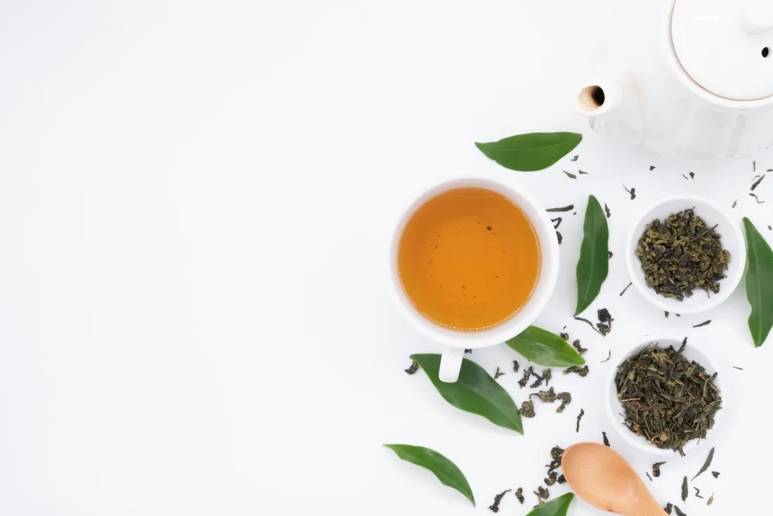 Green tea leaves steeping, with loose leaves scattered on a white background