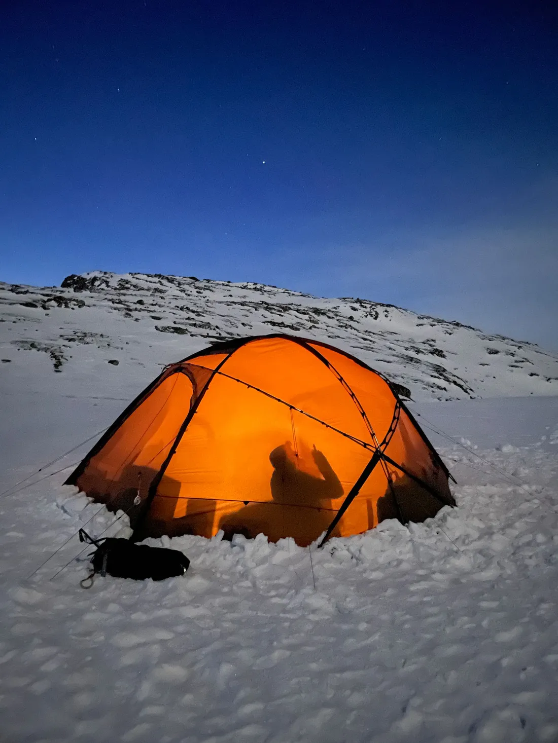 An orange tent pitched in a mountain valley