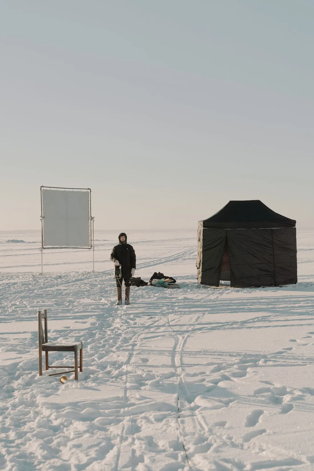 A person standing near a small tent on snow-covered alpine ground