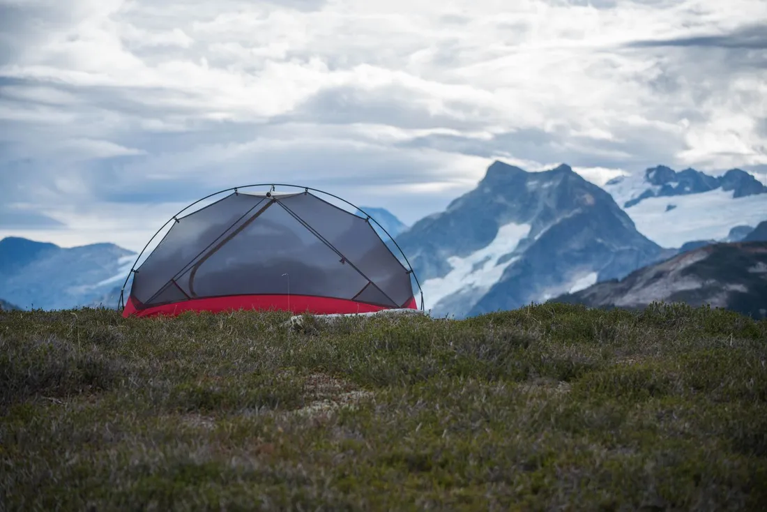 A black and red camping tent pitched in the mountains