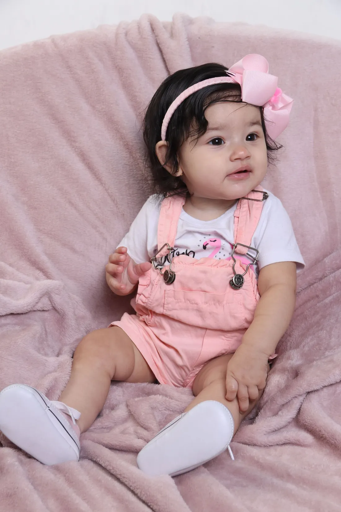A baby girl in a pink romper lying on soft pink textile