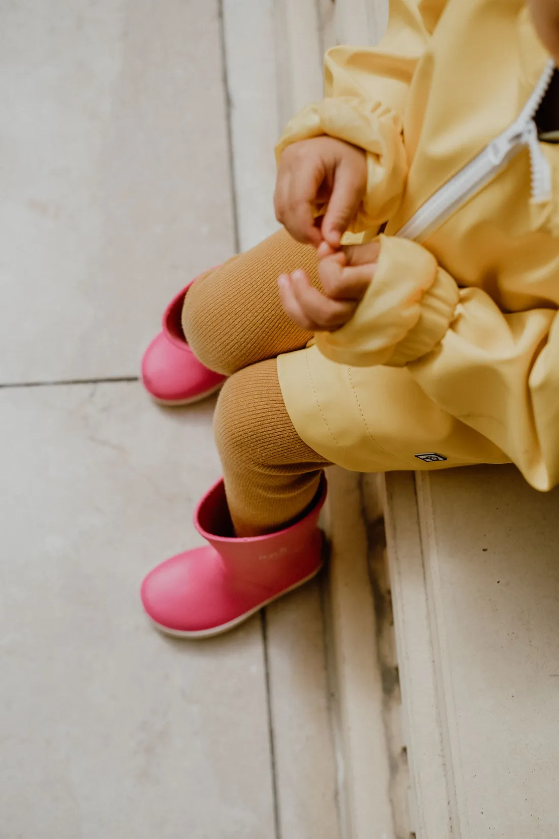 A child wearing a yellow raincoat and pink rain boots