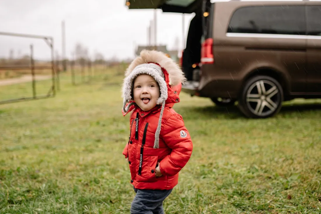A young child in a red puffer jacket enjoying a rainy day outdoors