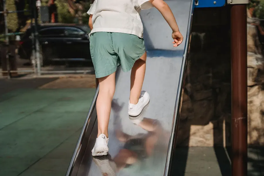 A kid climbing a slide in shorts and a t-shirt
