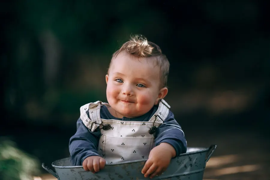 A charming baby in overalls smiling outdoors