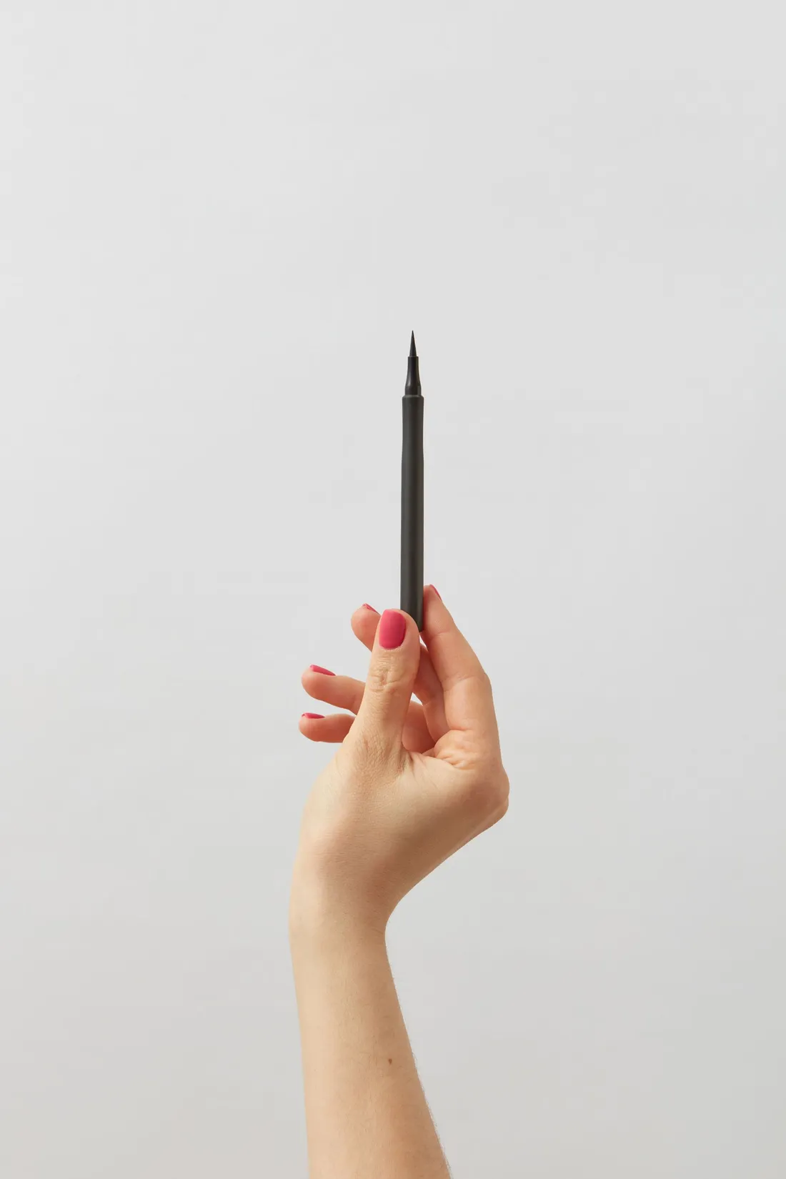 A hand holding a black eyeliner pen against a white backdrop