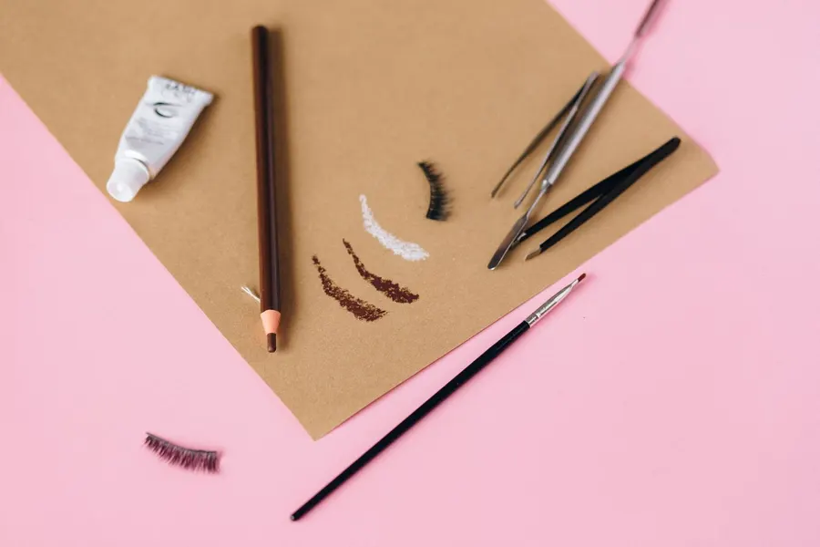 A collection of eyebrow makeup tools on a pink surface