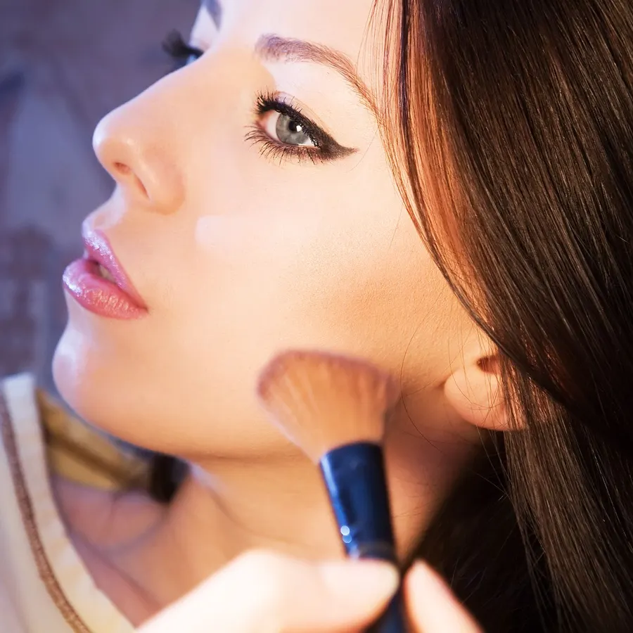 A woman applying blush with a makeup brush