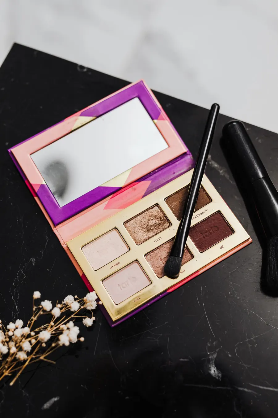 A stylish eyeshadow palette with brushes on a marble surface