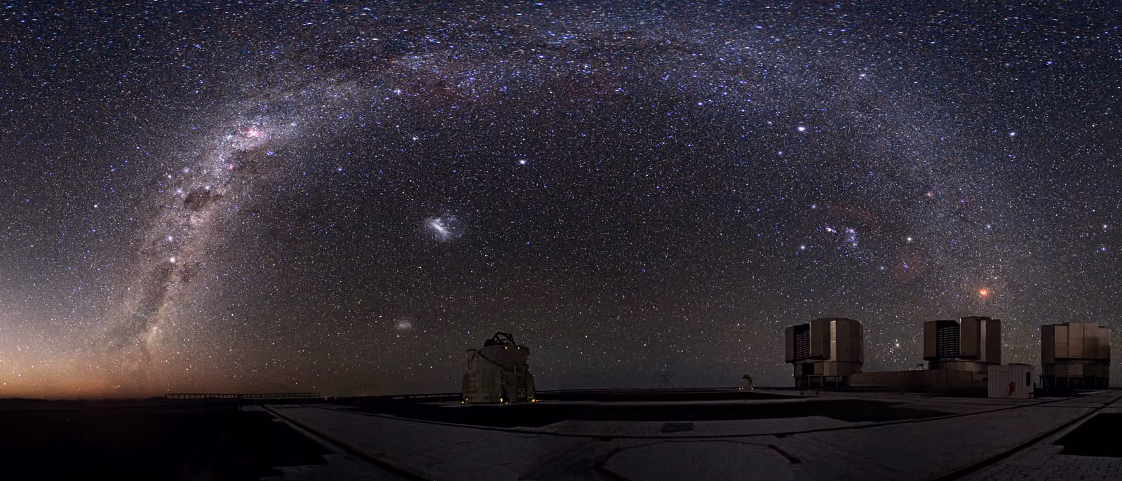 The Milky Way rising over a flat dark plateau, a low warm glow along the horizon.
