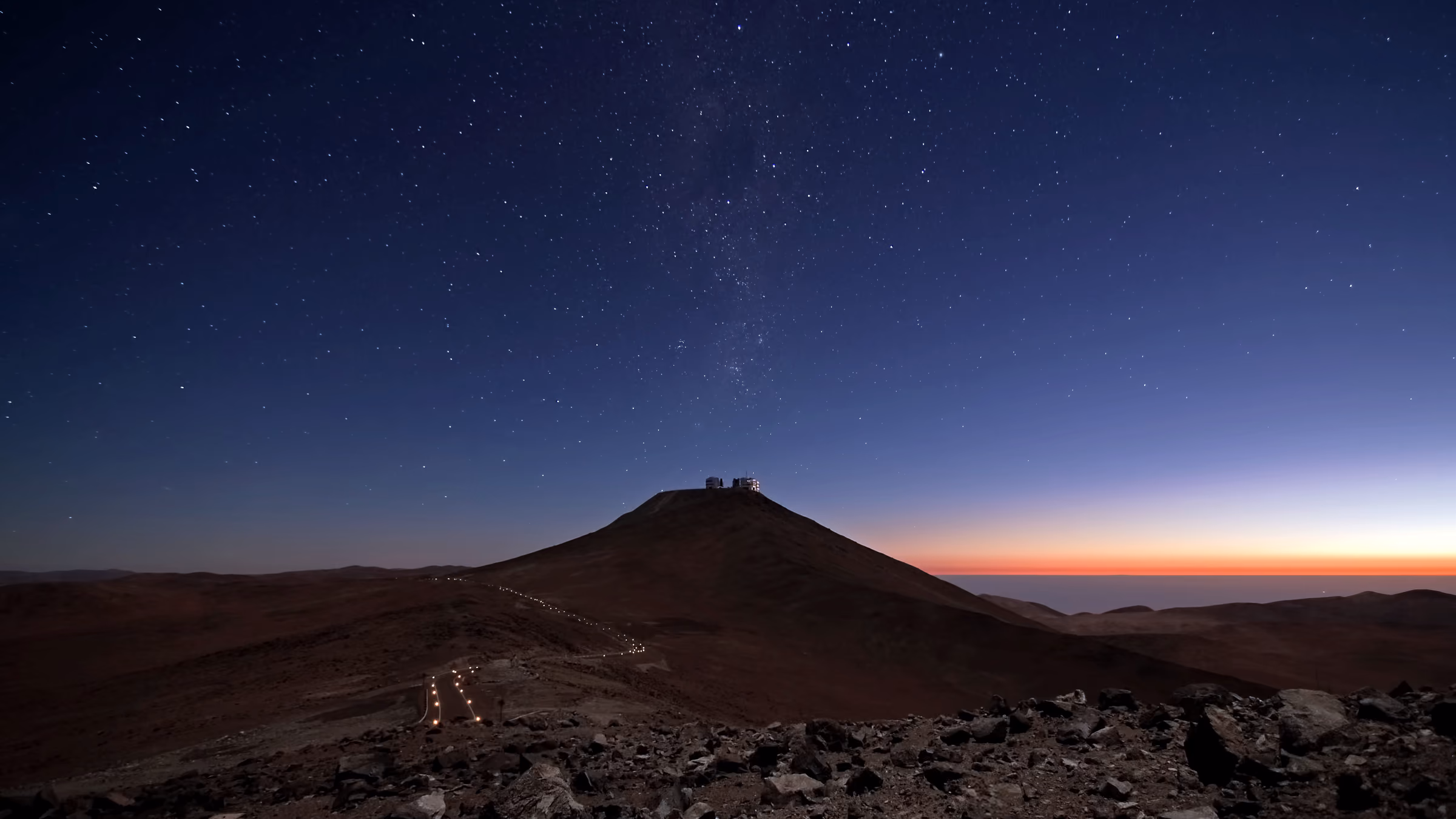 A ridge in high desert at last light, an observatory dome silhouetted on the summit, ochre band along the horizon.